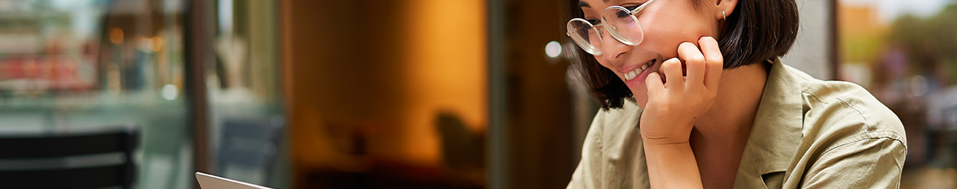 A woman sits in a café with her laptop and a coffee cup on the table.