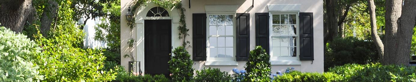 A white house with green vines and green plants and trees in its yard.
