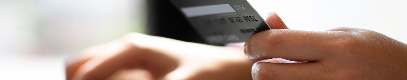 A person holds their credit card as they type their information into a laptop.