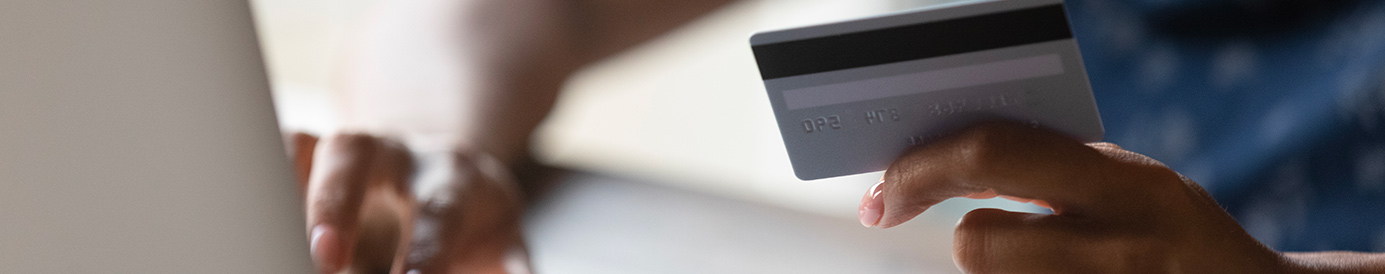 A woman types her credit card information into a computer. She is holding a credit card in one hand while typing with the other.