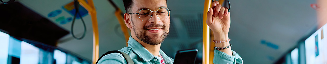 A man stands on a bus while looking at his phone.