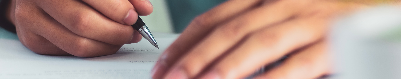 A person is signing a document. They have a black pen in their hand.