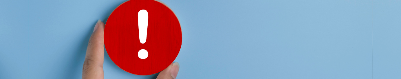 A woman’s hand positions a red disc with a white exclamation point on the front as it rests on a light blue background.