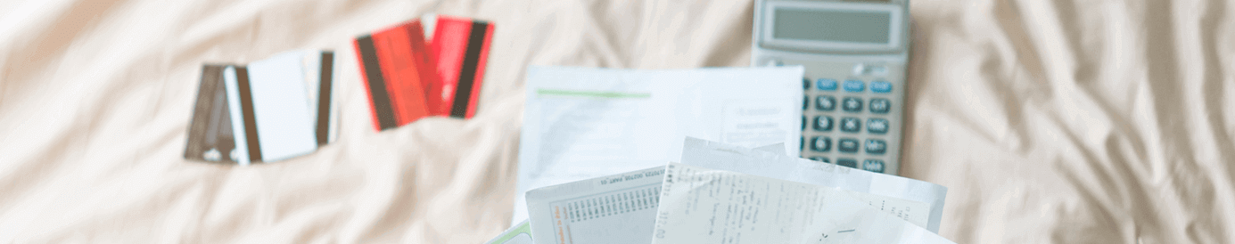 A calculator and 5 credit cards lay spread out on a bed. A person holds up a handful of financial papers above.