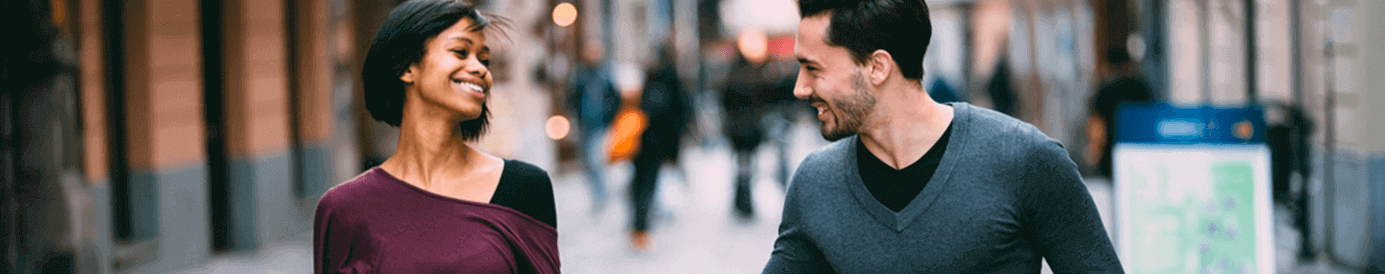 A man and woman are walking down a brick city street while holding hands.