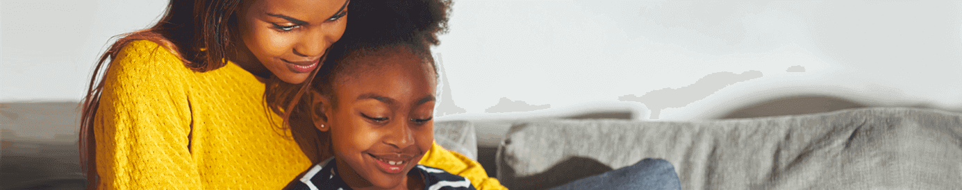 A mom and her daughter sit together on a couch watching a video on a tablet.