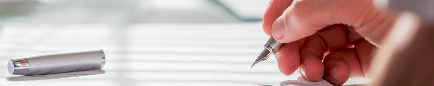 A person writing with a pen and paper on a green tabletop.