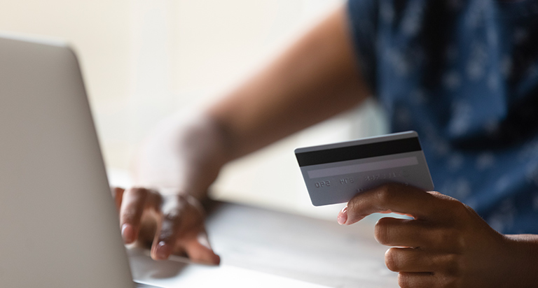 A woman types her credit card information into a computer. She is holding a credit card in one hand while typing with the other.