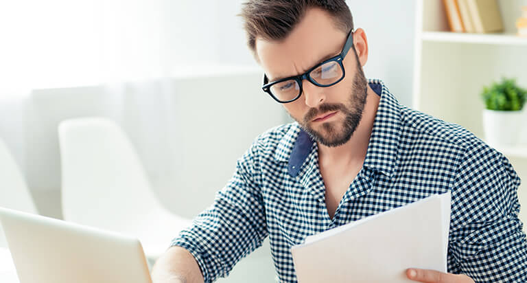 man reviewing a document while sitting at a desk with his computer open in front of him